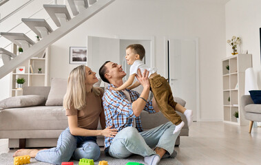 Cheerful young couple having fun with happy cute kid boy relaxing in modern house living room....