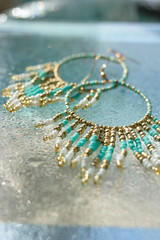 Turquoise earrings with sparkle drops of water on glass and blue backdrop under it, summer shiny jewelry in marine boho style