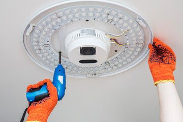 An electrician installs a chandelier on the ceiling. Hands of an electrician installing or...