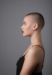 Woman with shaved hairstyle, posing over grey background. Vertical shot.