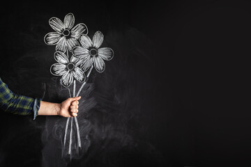 Man holds a bouquet of flowers drawn on the blackboard with a chalk. Spring, Woman's day or...