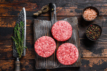 Raw steak burgers patties with ground beef and thyme on a wooden cutting board. Dark Wooden...