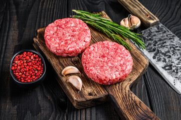 Raw steak cutlets with mince beef meat and rosemary on a wooden cutting board with meat cleaver....
