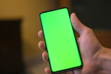 Isolated human hand holding a green screen smartphone,hi tech addiction concept