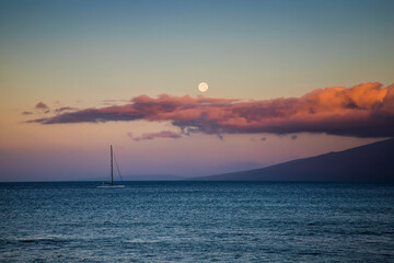 Full Moon Setting Behind Pink Clouds at Daybreak over Ocean with Boat and Island - 429099785