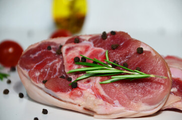 pieces of raw pork steaks, with ingredients for cooking, served on woodenboard. with rosemary, cherry tomatoes, black pepper and olive oil on the table Concept of food preparation on white background