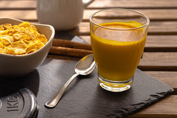 Indian breakfast of golden milk with curcuma and cinnamon stick accompanied by cornflakes on a wooden table on a sunny and relaxing day, Indian food concept.