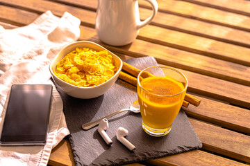 selective focus Breakfast on wooden table with mobile phone headset with golden milk food with turmeric and cinnamon accompanied by cereals Indian food concept energy