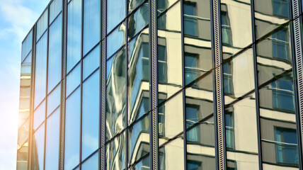 Blue sky reflection in glass facade of building. View of office building windows close up with sunrise, reflection and perspective.. Glass facade on a bright sunny day with sunbeams on the blue sky. 