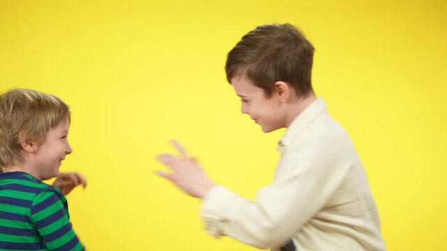 Laughing little brothers having fun fighting at yellow background. Positive Caucasian boys imitating fight. Relaxation and childhood concept