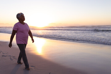 Senior african american woman walking on the beach during sunset - Powered by Adobe