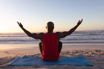 Rear view of senior african american man with arms wide open practicing yoga at the beach