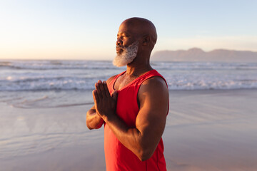 Senior african american man with folded hands meditating and practicing yoga at the beach - Powered by Adobe