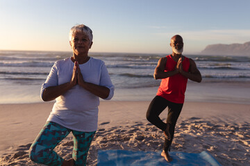 Senior african american couple with folded hands meditating and practicing yoga together at the beac