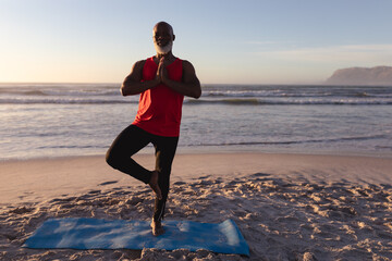 Senior african american man with folded hands meditating and practicing yoga at the beach