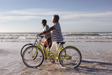 Happy senior african american couple with bicycles walking together on the beach - Powered by Adobe