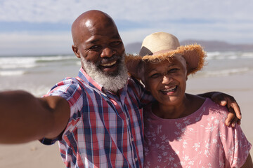 Portrait of happy senior african american couple taking a selfie at the beach - Powered by Adobe