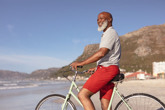 Senior african american man sitting on bicycle smiling on the beach