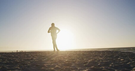 African american man running on beach, exercising outdoors in beach in the evening