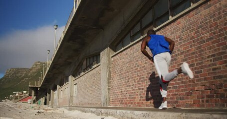 African american man running on pavement, exercising outdoors on sunny day