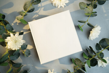 Blank canvas frame, white flowers and plant branches. Mockup poster on romantic floral background. Top view.
