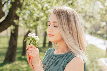Sunny sensual portrait of a beautiful girl who sniffs an apple tree flower with her eyes closed