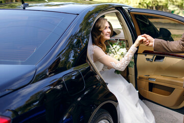 Groom helps happy young bride to get out of wedding car