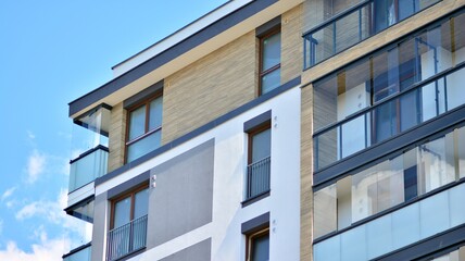 Obraz premium A fragment of modern architecture, walls and glass. Windows and balconies of a residential building against a blue sky. Detail of New luxury house and home complex. Part of city real estate property a
