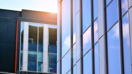 Blue sky reflection in glass facade of building. View of office building windows close up with sunrise, reflection and perspective.. Glass facade on a bright sunny day with sunbeams on the blue sky. 