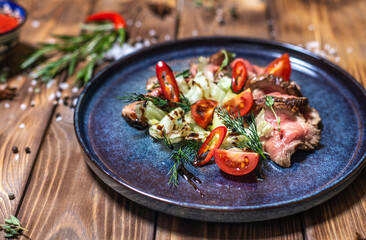 Beef tenderloin fried on fire with herbs, seasoned with spices, tomatoes. Wooden brown background decorated with rosemary, spices.