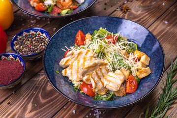 Chicken salad, sliced vegetables with fresh arugula are on a wooden table.