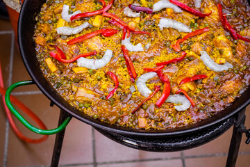 Close up of a tasty Spanish typical paella with prawns, peas, chicken and red pepper in a base of rice and vegetables. Traditional Spanish food. Paella cooked in a paellero. Paella ready to eat.