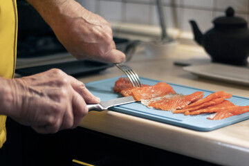 Hand cuts red fish, trout or salmon into slices on a cutting board.