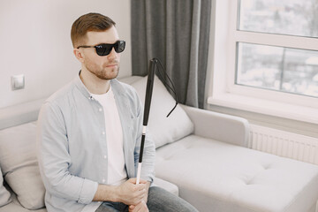 Visually impaired man sitting on the couch with stick