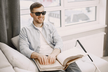 Blind young man reading braille book on couch