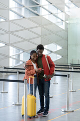 Fototapeta na wymiar First trip after covid-19 end. Young black couple with luggage ticket in empty airport wait for check-in, use smartphone to boarding pass registration online happy to travel again with no corona virus