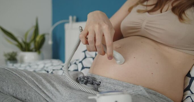 Young pregnant woman use pocket ultrasound doppler to check baby heart rate. The girl runs the sensor over her stomach, trying to detect the baby's pulse.