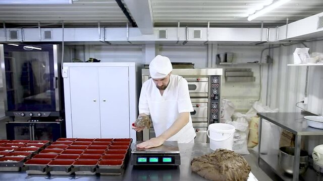 Small mini bakery. Slow motion. A bearded male baker greases the surface of a scale with butter for placing bread dough.