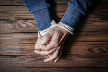 a Hands tied with a rope life-threatening on a wooden background. Slavery in business is human abuse.
