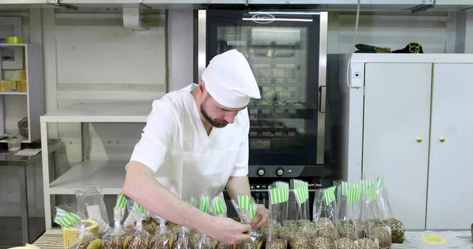 Small home bakery. A male baker in a white uniform is packing fresh bread into packaging bags.