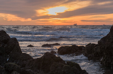 Sunset from the beach in Mazatl?n Mexico with boats in the distance and rocky coast in the foreground