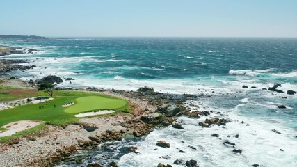 Outdoor nature adventure. 4K cinematic aerial view of green golf course at the scenic rocky coast and beautiful shore of deep green Pacific ocean, with waves crashing on the picturesque rocks, USA