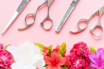 Professional scissors for a hairdresser and flowers on pink background close-up.