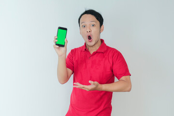 Wow face of Young asian man smiling when showing green screen of smartphone in studio background
