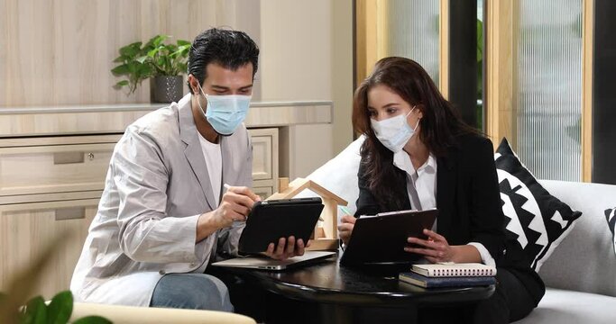 Beautiful woman real estate agent offering and showing online presentation on laptop in office to handsome man. People wearing face mask protective corona virus.