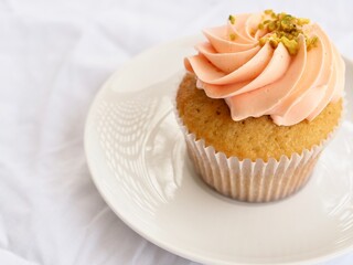 Pretty pink cupcake on a white plate, on a white textured background