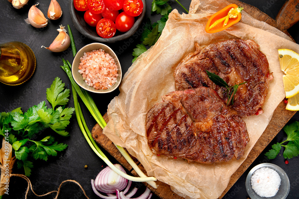 Wall mural delicious prepared meat steaks with seasoning and herbs on dark background.