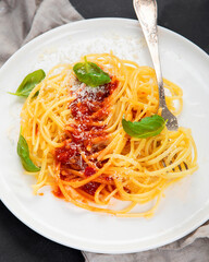 Delicious appetizing Italian pasta spaghetti with tomato sauce, parmesan and basil on a plate on a gray background. Top view, copy space