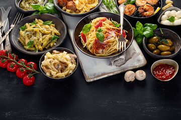 Assortment of Italian pasta with traditional sauces for dinner on dark background.