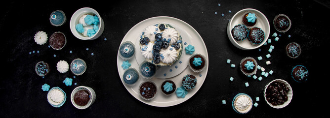 Delicious cake and cupcakes in blue on dark background. Table setting for celebration.